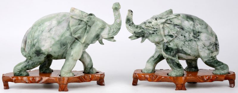 Een paar olifanten van gesculpteerd jade op houten voetstukjes.