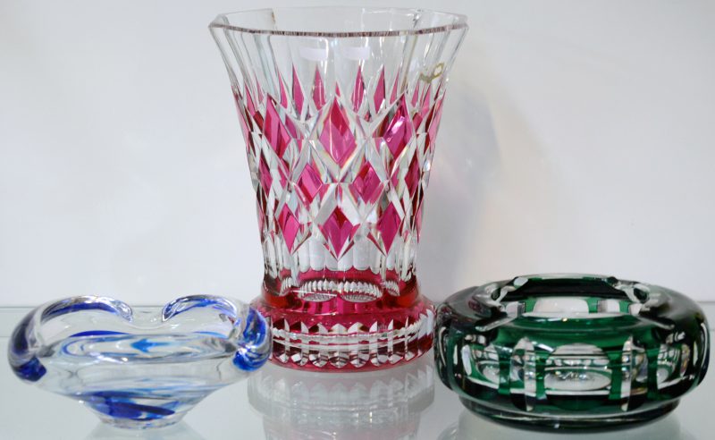 Een lot kristallen voorwerpen, bestaande uit een blauwe en een groene asbak en een vaas met roze ruitmotieven. De laatste twee van Val St. Lambert.