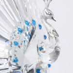 “De pauw”. Een beeldje van geslepen kleurloos kristal en sterling zilver op sokkel van kunststof naar een ontwerp van Adi Socker. Genummerd 5151/10.000 In originele doos met certificaat en begeleidend boekje.