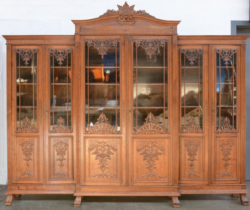 Een geebeeldhouwde bibliotheekkast met drie maal twee deuren met fraaie versieringen over het glas en met een acanthusblad in de kuif.