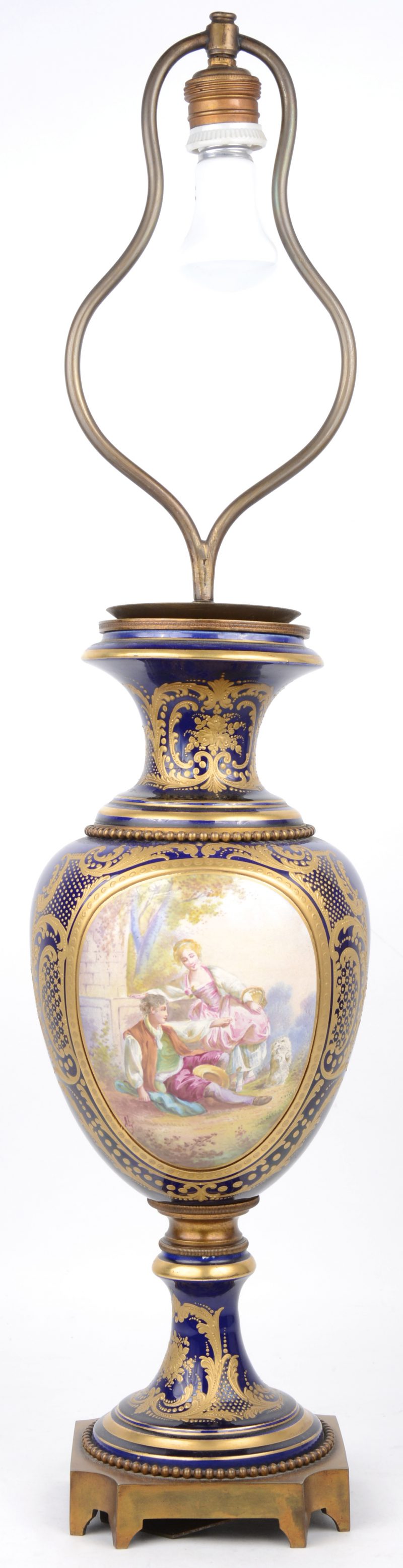 Een lampenvoet van kobaltblauw en verguld Sèvresporselein met een handgeschilderd decor van een koppel in een landschap en met koperen monturen. Draadstang te vervangen.