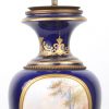 Een lampenvoet van kobaltblauw en verguld Sèvresporselein met een handgeschilderd decor van een koppel in een landschap en met koperen monturen. Draadstang te vervangen.