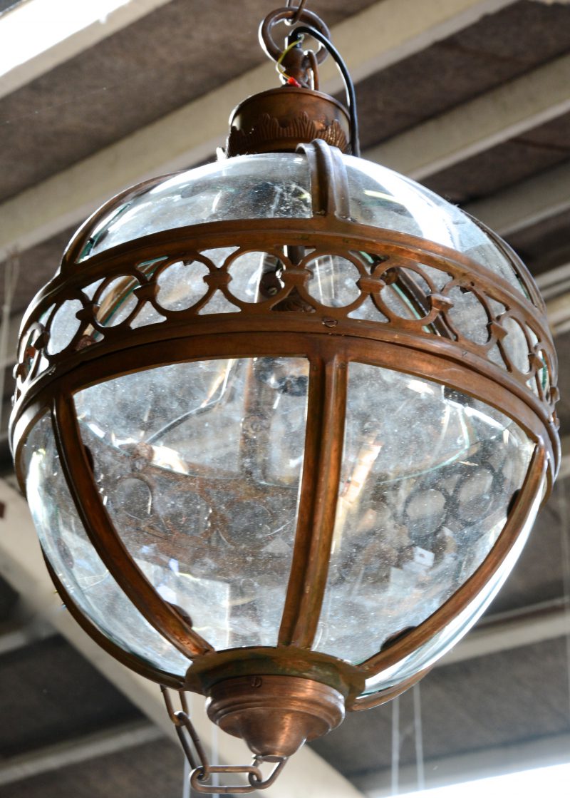 Een balvormige hanglantaarn van brons en glas.
