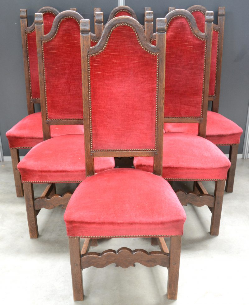 Een reeks van zes sobere eikenhouten stoelen, bekleed met rood fluweel.