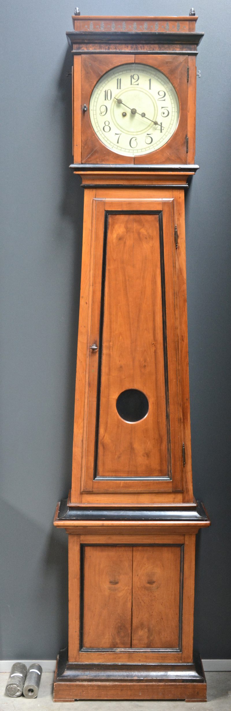 Een staande klok van notenhoutfineer met zwartgelakte details. XIXe eeuw. Werkende staat. Compleet met slinger en gewichten.
