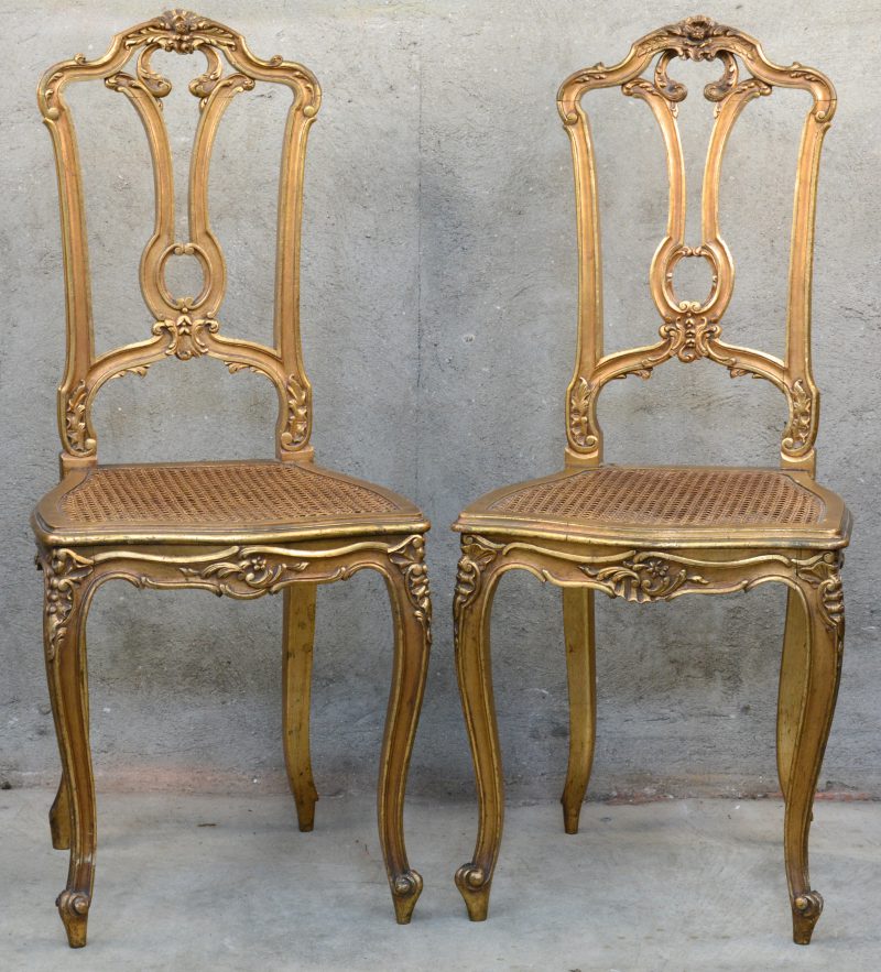 Een paar goudgepatineerde stoeltjes in barokke stijl met gecanneerde zit.