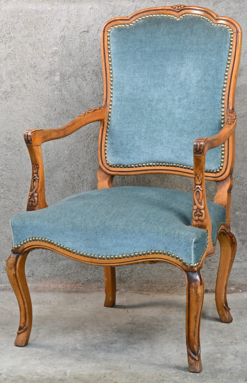 Een fauteuil-à-la-Reine van gebeeldhouwd notenhout, bekleed met blauw fluweel.