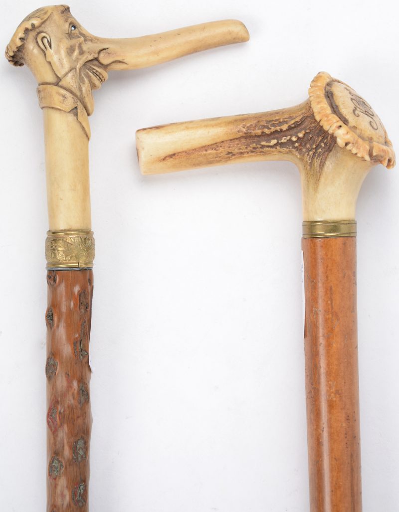 Twee houten wandelstokken met messingen monturen en met handvat van gesculpteerd reeëngewei, waarbij één in de vorm van een karikaturaal mannenhoofd en de andere met gegraveerde initialen en datum 1885.