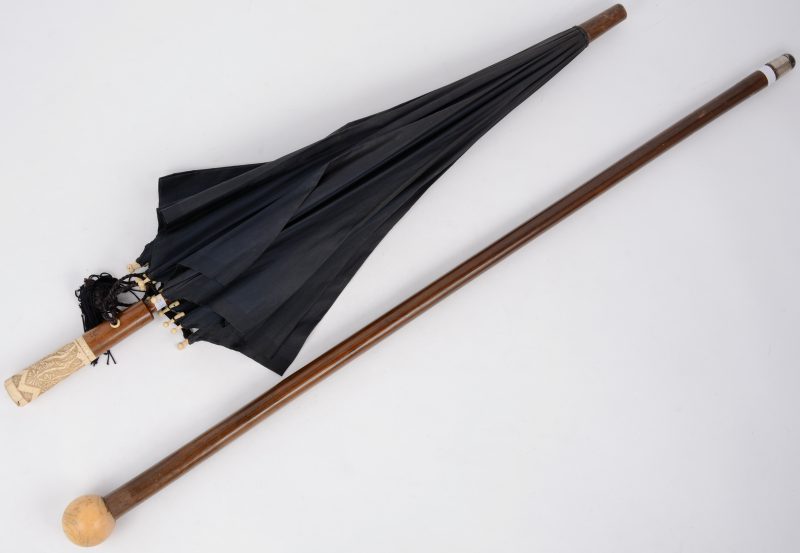 Een houten wandelstok met een bolvormig handvat van ivoor en een antiek paraplu met gesculpteerd ivoren handvat.