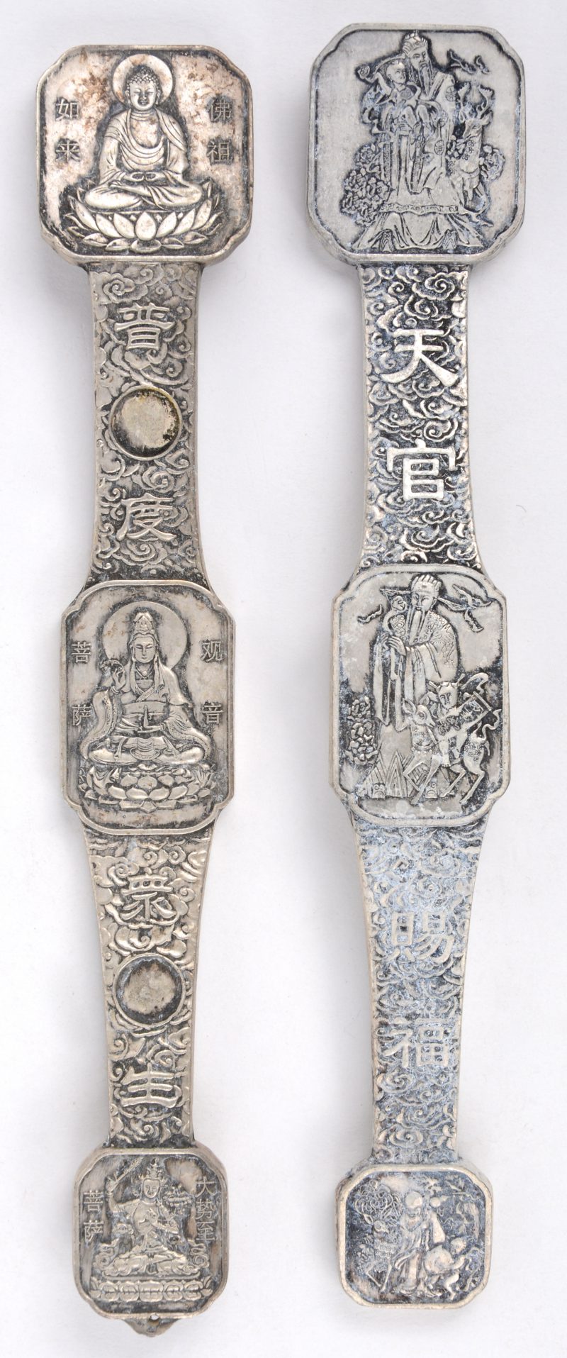 Een paar ruyi’s van wit metaal met voorstellingen van Boeddha.