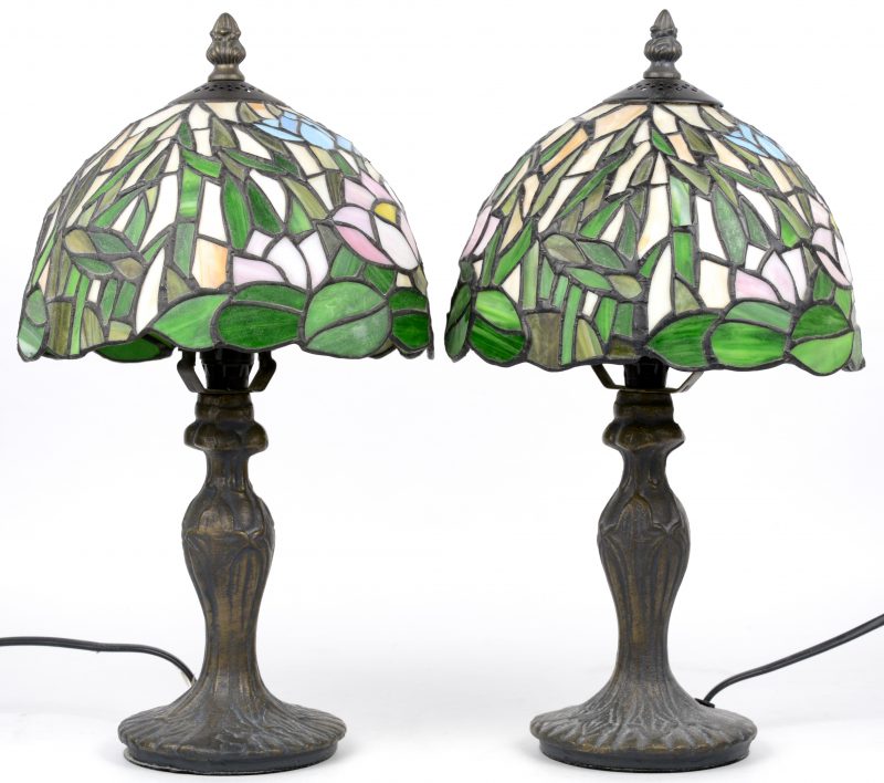 Een paar bronzen schemerlampjes met kapjes van glas in lood in de stijl van Tiffany.