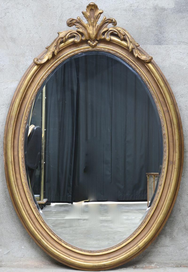 Een ovale spiegel van verguld hout met een acanthusblad in de kuif.