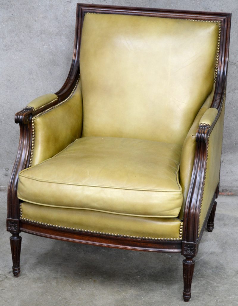 Een notenhouten fauteuil in Lodewijk XVI-stijl met olijfgroene lederen bekleding.
