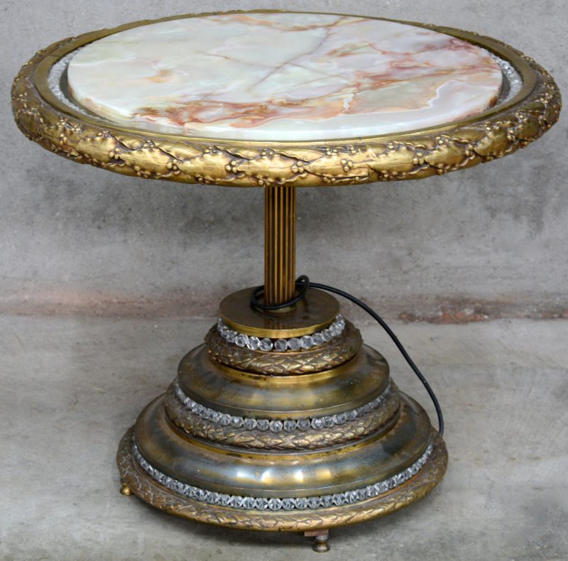 Een bronzen salontafel met een rond onyxen blad, versierd met kristallen steentjes.