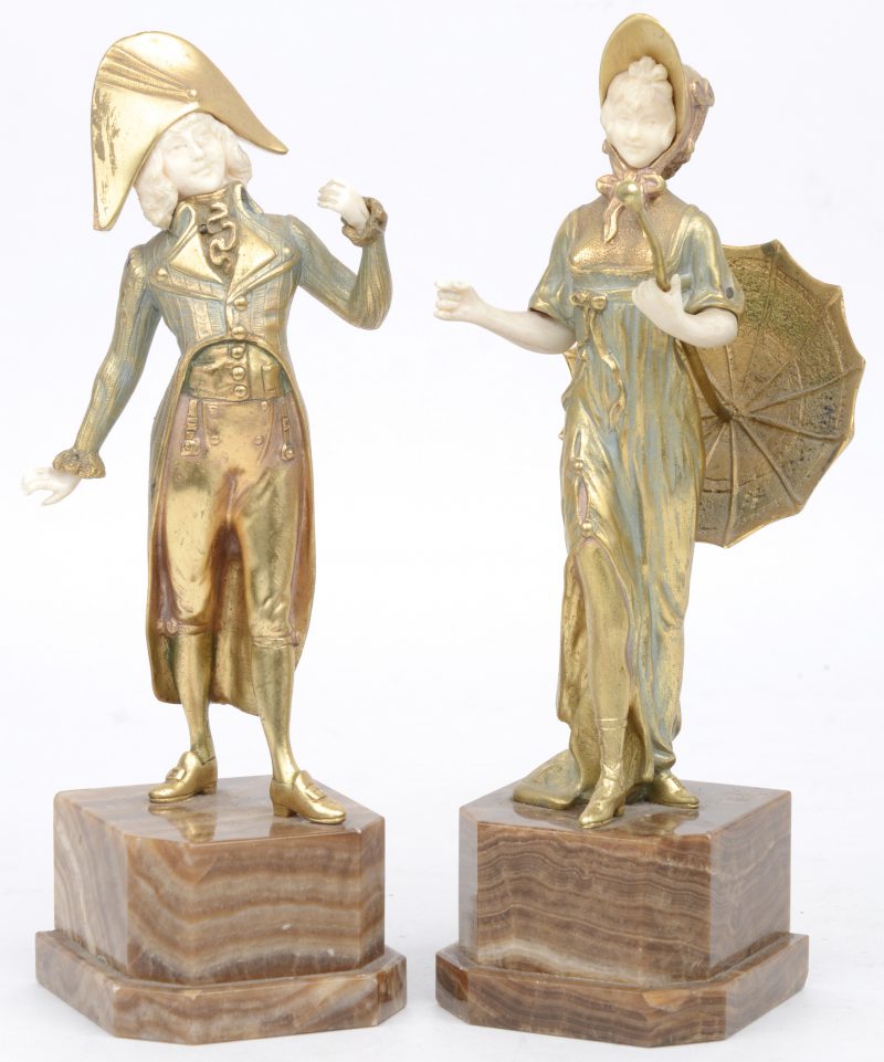 “Dame in uniform” et “Dame met parasol”. Een paar bronzen beeldjes met ivoren hoofdjes en handjes en op onyxen voetstukken.