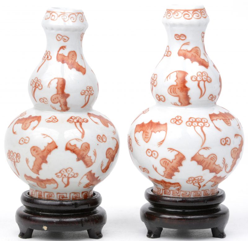 Een paar kleine kalebasvaasjes van Chinees porselein met een oranje decor van vleermuizen. Onderaan gemerkt. Met twee houten sokkeltjes.