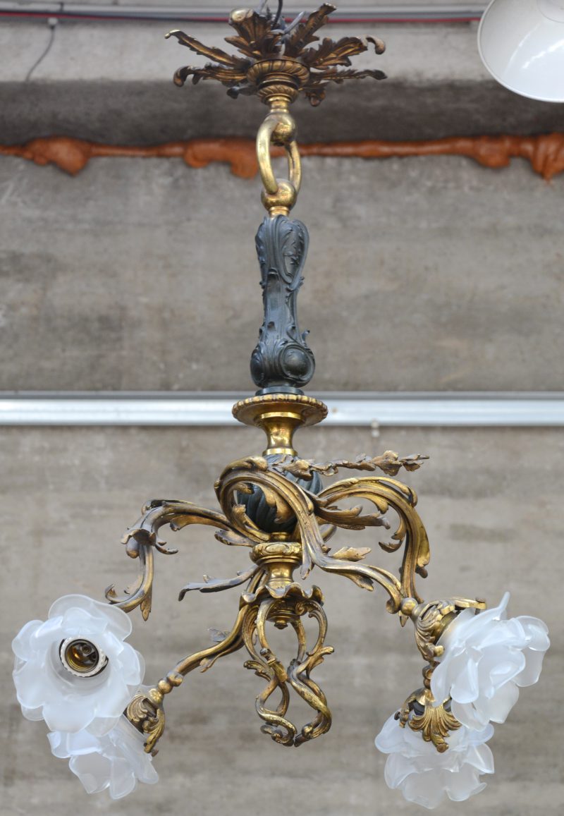 Een bronzen luchtertje in rococostijl met vier lichtarmen in vegetale vorm met glazen bloemvormige kapjes. (Eéntje beschadigd). XIXe eeuw.