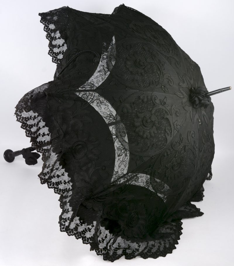 Een parasol van zwarte Chantilly kant en bloemenborduursel, de handgreep van gebeeldhouwd hout. Omstreeks 1900.