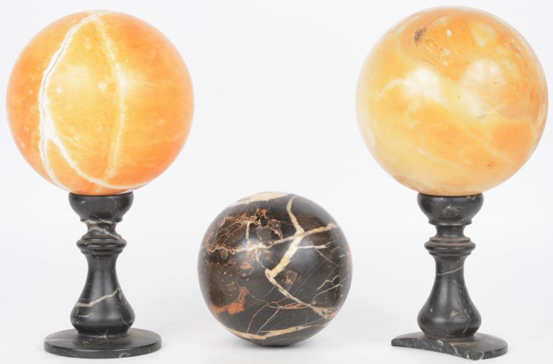 Een lot van twee grote bollen en een kleinere, resp. van oranje en zwart marmer. We voegen er twee zwart marmeren staandertjes aan toe. (Eén voet beschadigd).
