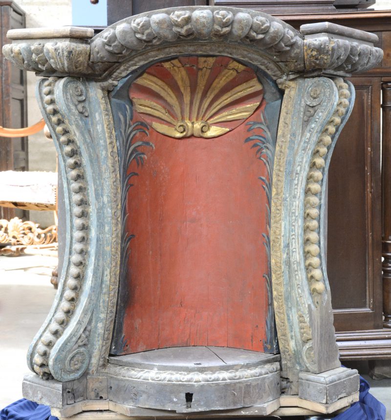 Een XVIIIe eeuwse beeldenconsole van gebeeldhouwd en gepolychromeerd hout, versierd met een rondboog. Het binnenwerk roterend met drie verschillende nissen.