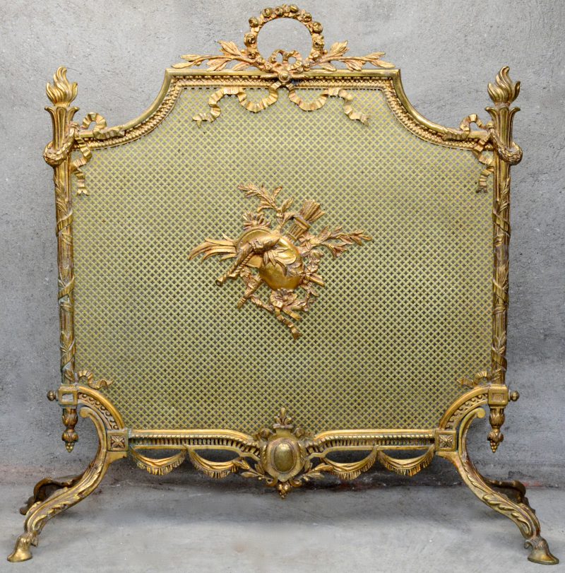 Een verguld bronzen haardscherm in Lodewijk XVI, versierd met strikken, guirlandes en een wapen met doedelzak en een fakkel.