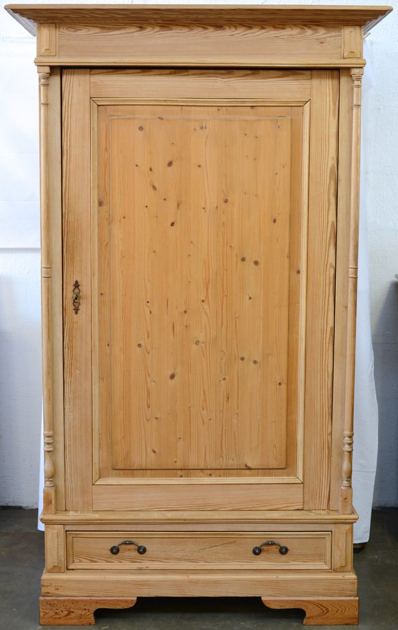 Een bleek houten ééndeursgarderobe met twee gedraaide zuiltjes.
