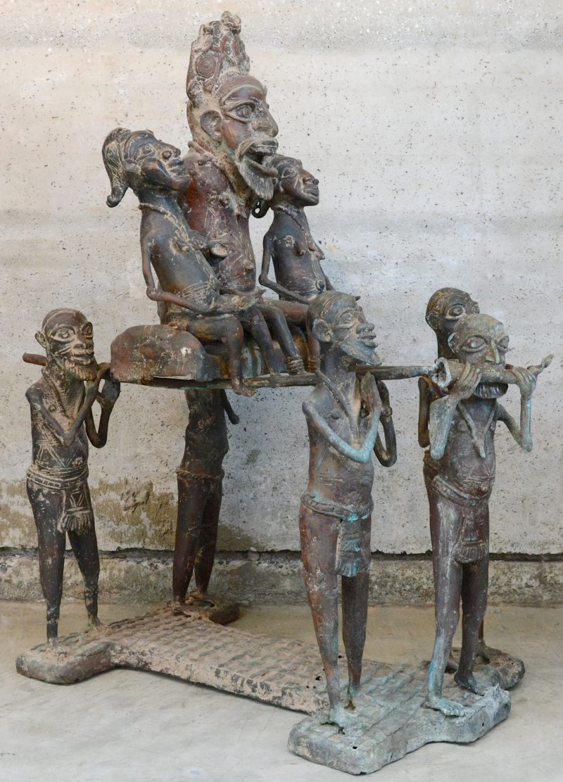 Een Afrikaanse groep van brons met een voorstelling van een stamhoofd, vergezeld door twee vrouwen, gedragen door zijn volgelingen.