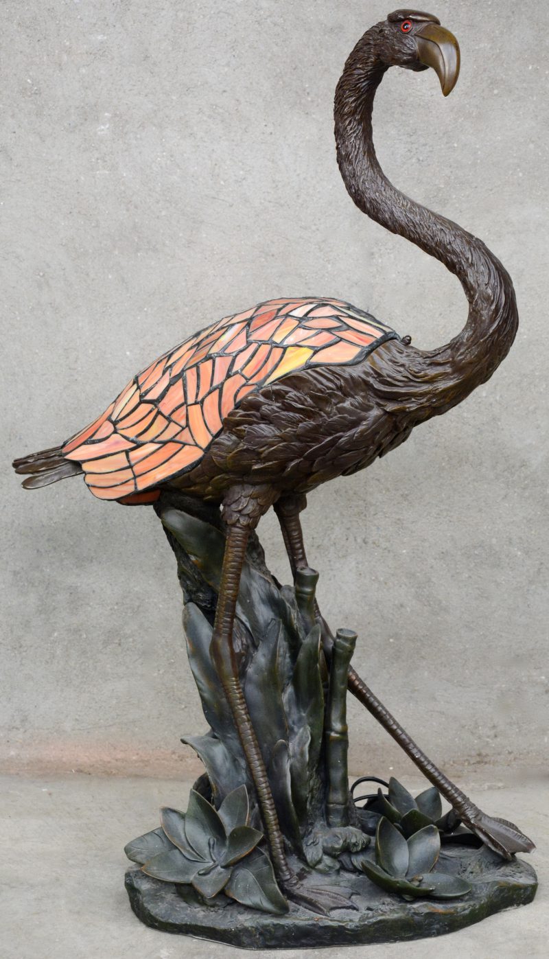 Een lamp van bruingepatineerd kunststof in de vorm van een Flamingo met vleugels van glas in lood als kap.