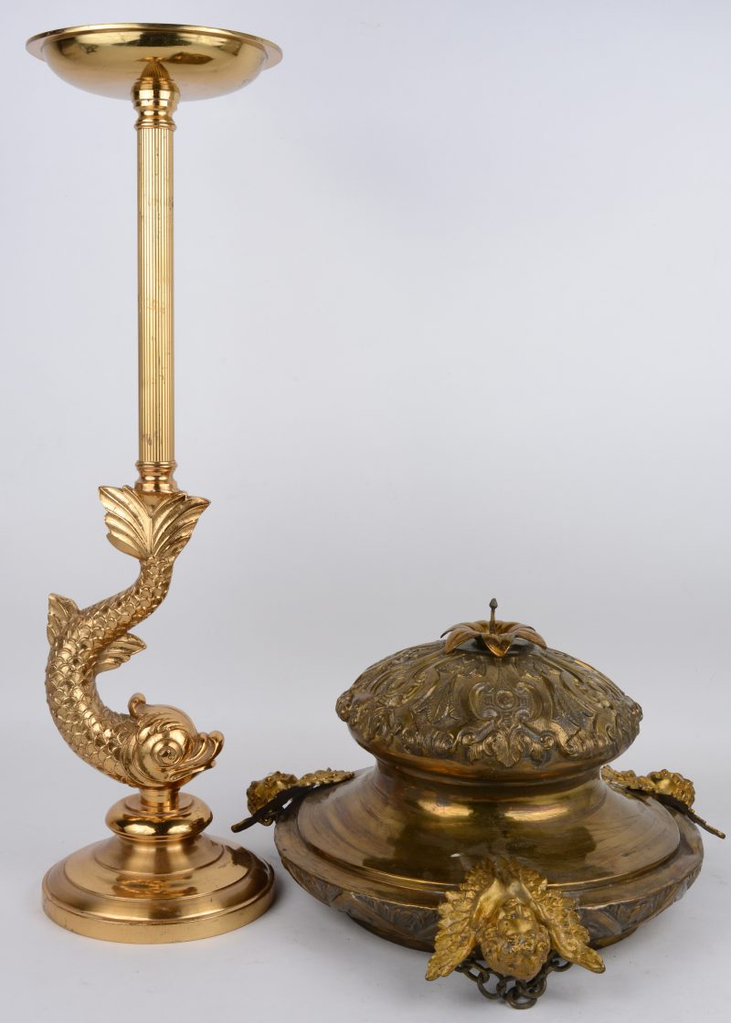 Twee voorwerpen van geel koper, bestaande uit een gedreven godslamp en een massieve staander in de vorm van een barokke dolfijn.