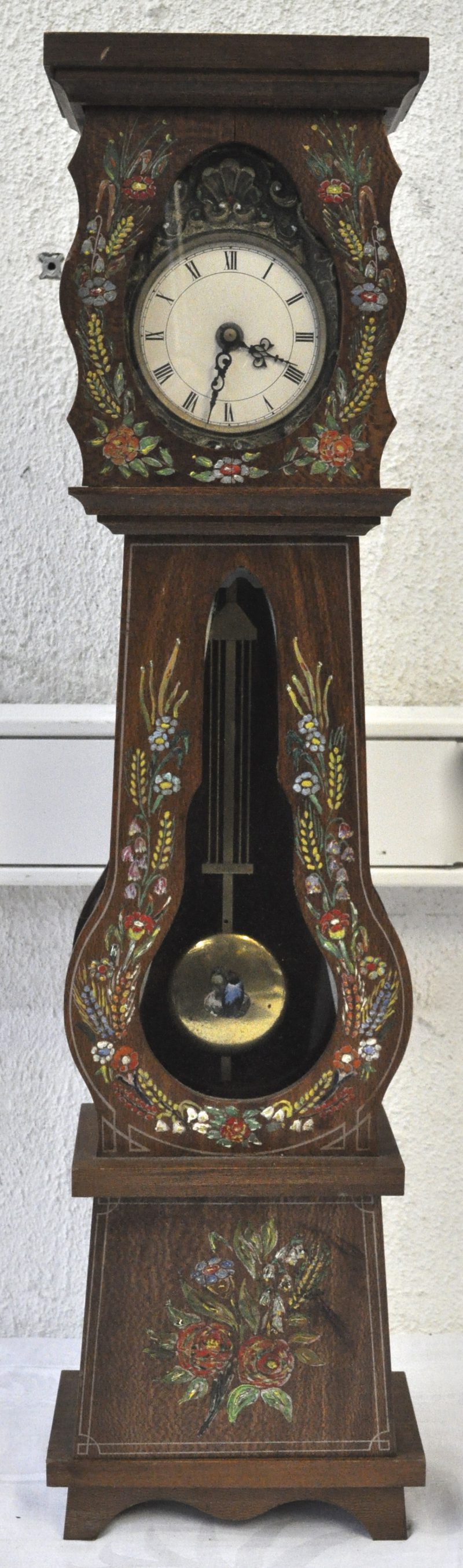 Een miniatuur staande klok met een handgeschilderd meerkleurig bloemendecor versierd.
