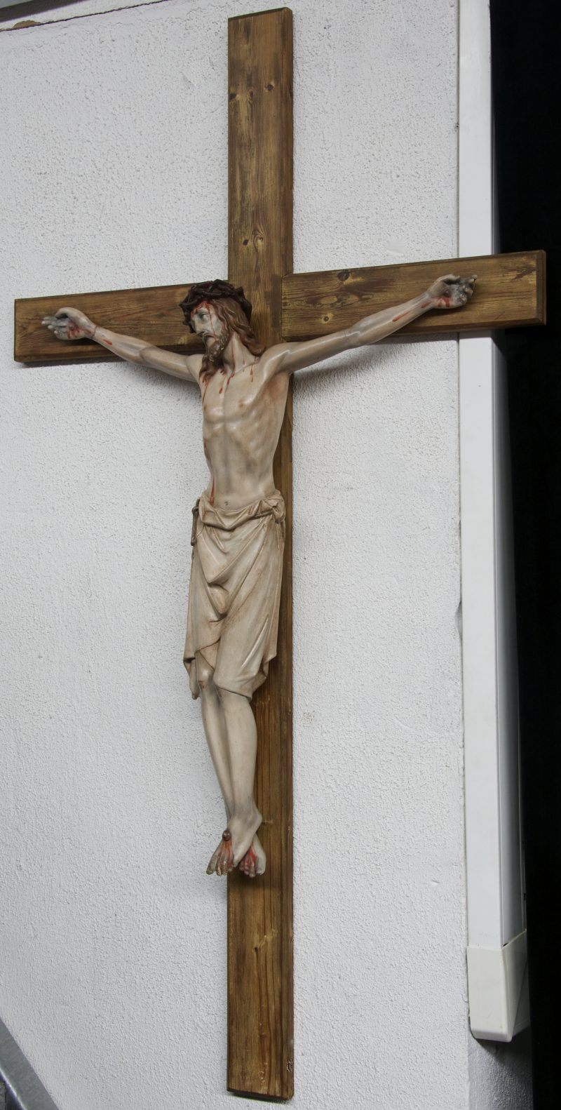 Een groot houten kruisbeeld met een Christus van polychroom gips. Restauratie aan de arm. Eind jaren ‘30.