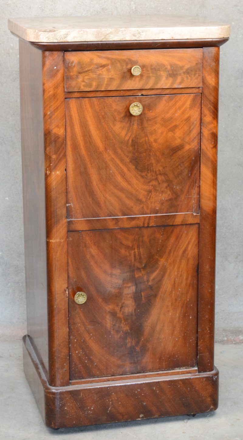 Een nachtkastje van mahoniehoutfineer met een deurtje onderaan, een compartiment met klapblad in het midden en een lade onder het beige marmeren blad. XIXe eeuw. Schilfer aan het blad.
