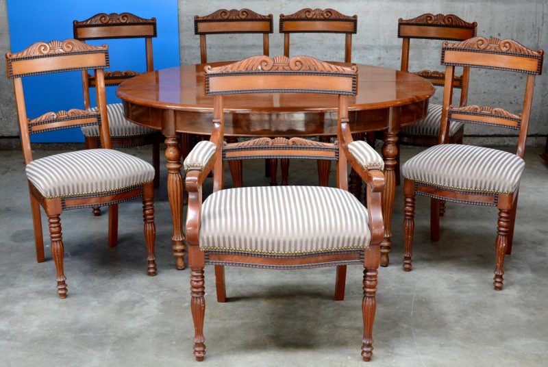 Een ovale tafel van mahoniehoutfineer met zes gecanneleerde poten. Verlengbaar met vijf bladen tot 350 cm. Met zes bijpassende stoelen en een armstoel.