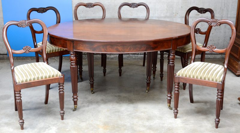 Een verlengbare mahoniehouten tafel met zes bijpassende stoelen in Louis-Philippestijl. Met drie verlengbladen. Eén stoel te restaureren.