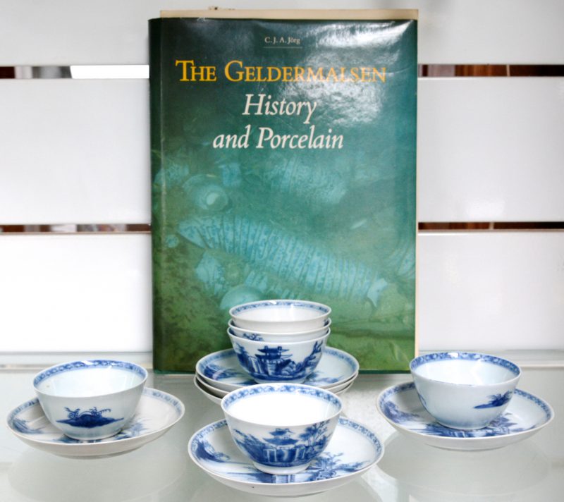Een reeks van zes theekopjes met schoteltjes van Chinees porselein met een blauw landschapsdecor. Omstreeks 1750. Afkomstig van het schip “de Geldermalsen”, gezonken in 1752 en geborgen in 1985. Het lot destijds aangekocht in de ‘Naking cargo”- veiling bij Christie’s te Amsterdam. We voegen er een boek over de Geldermalsen aan toe.