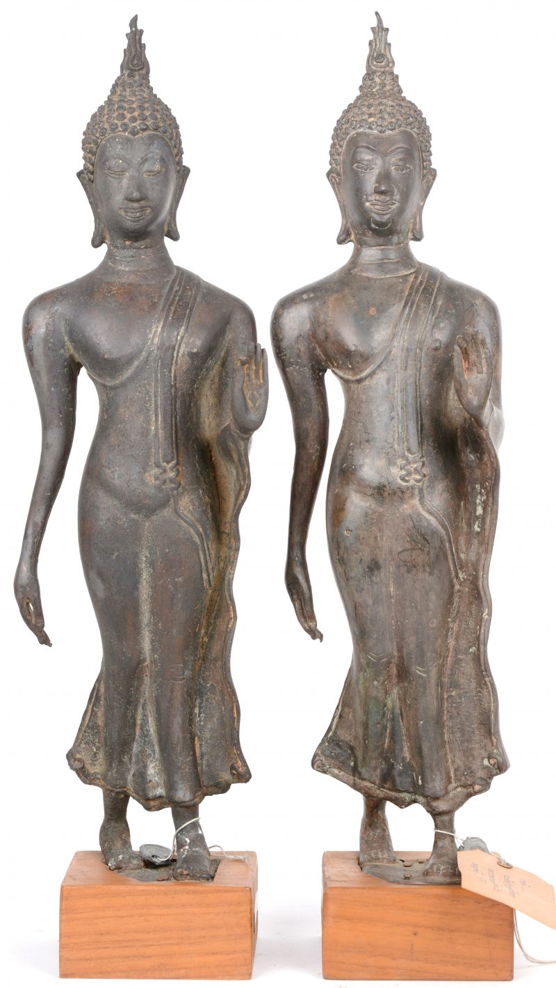 Twee bronzen staande Thaise Boeddha’s op een houten voetstuk.
