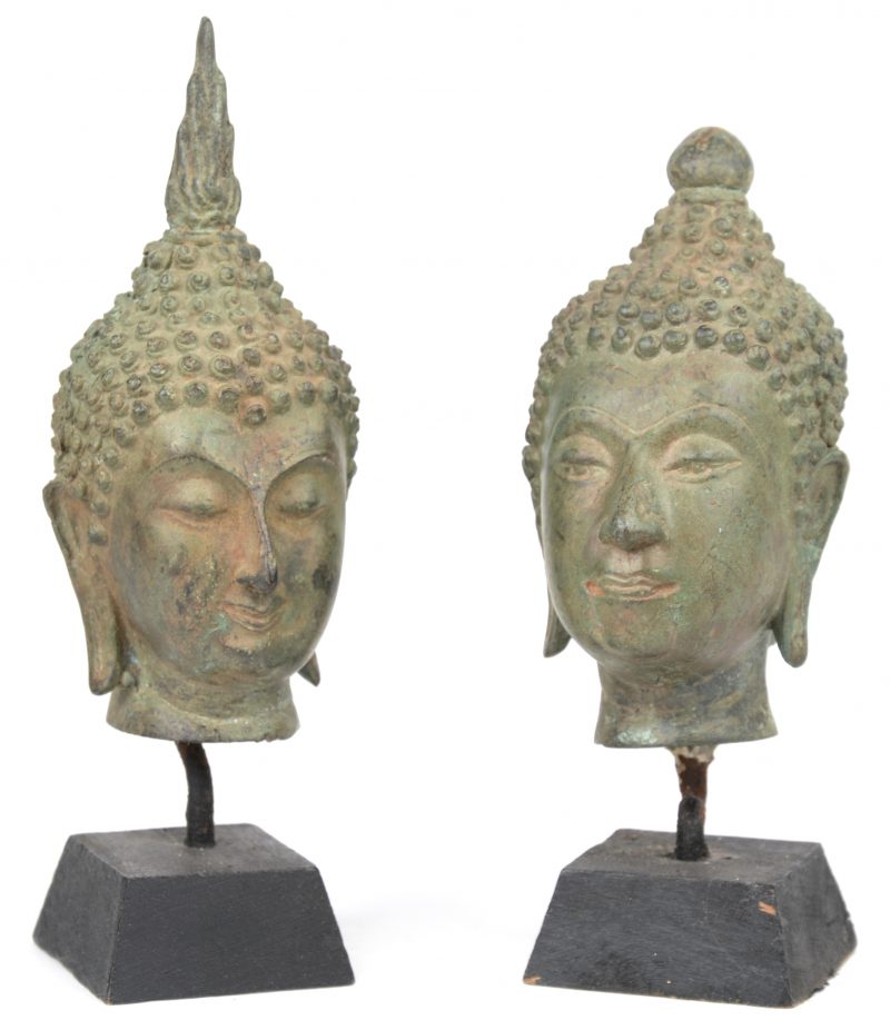 Twee Thaise Boeddhahoofdjes van brons op een houten sokkeltje.