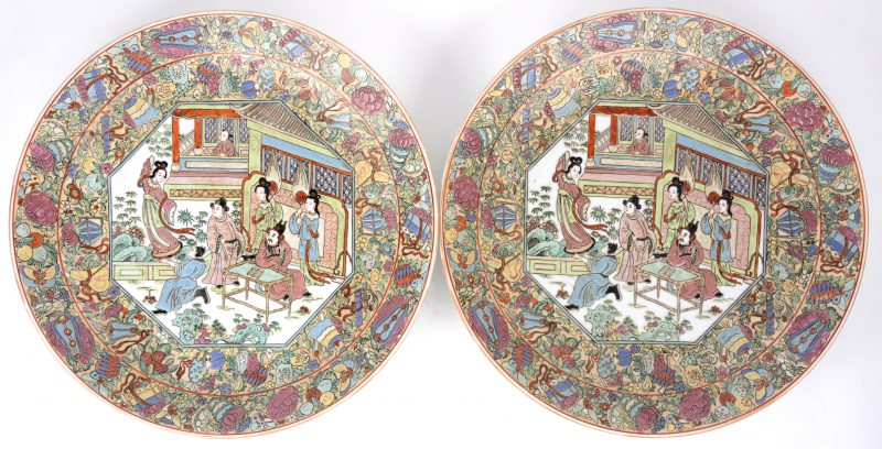 Een paar Chinese schotels van meerkleurig porselein met een decor van de keizerlijke hofhouding, omring door bloemen in reliëf. Onderaan gemerkt.