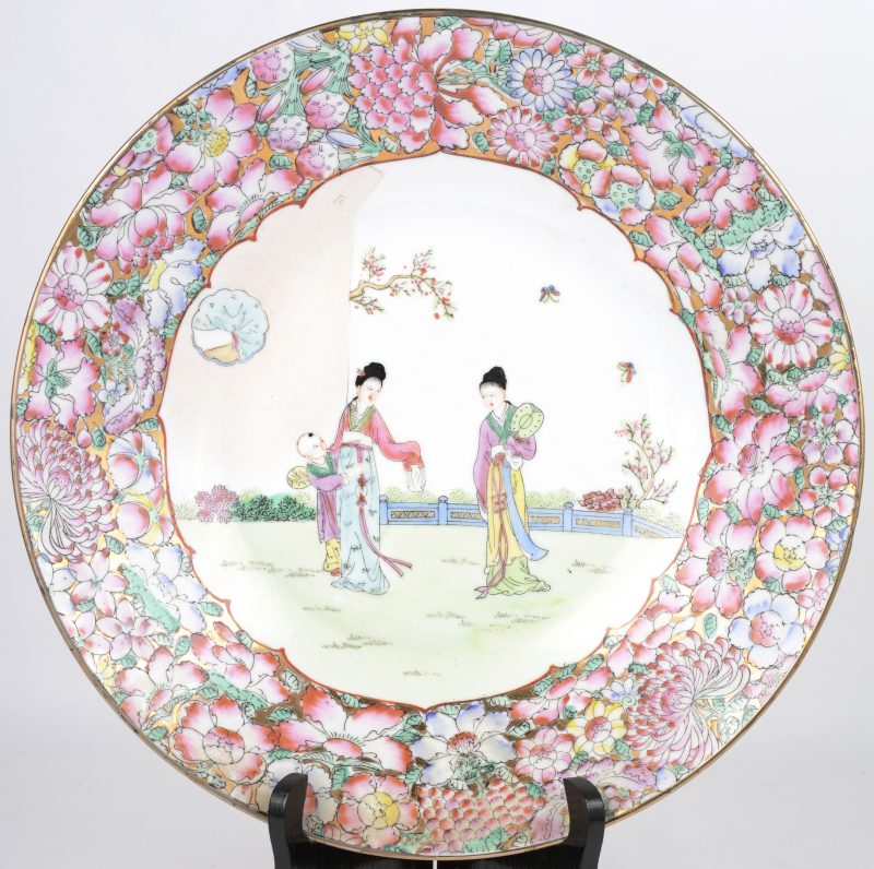 Een schotel van Chinees porselein met een meerkleurig decor van lange lijzen en pioenen.