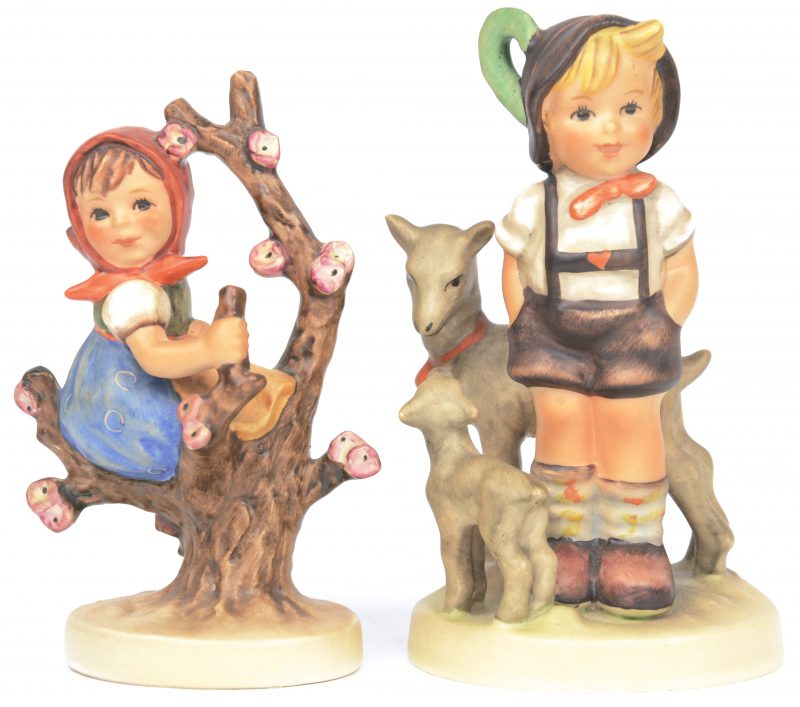 “Meisje op tak” en “Jongetje met twee geitjes”. Twee beeldjes van meerkleurig porselein uit de reeks van M.I. Hummel. Onderaan gemerkt.