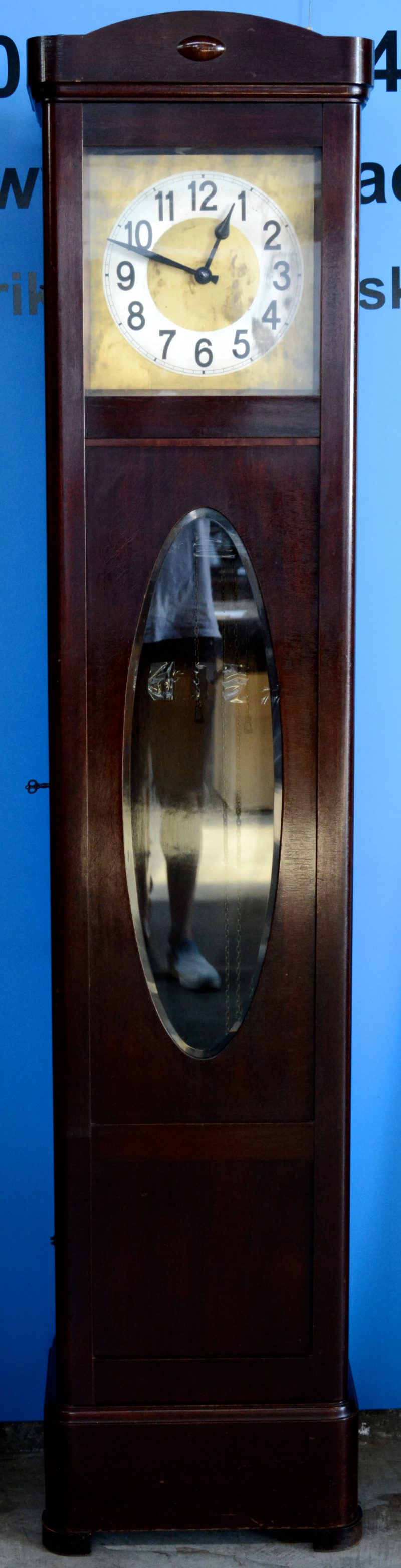 Een staande klok in houten kast met een koperen wijzerplaat. Compleet met slinger en gewichten.