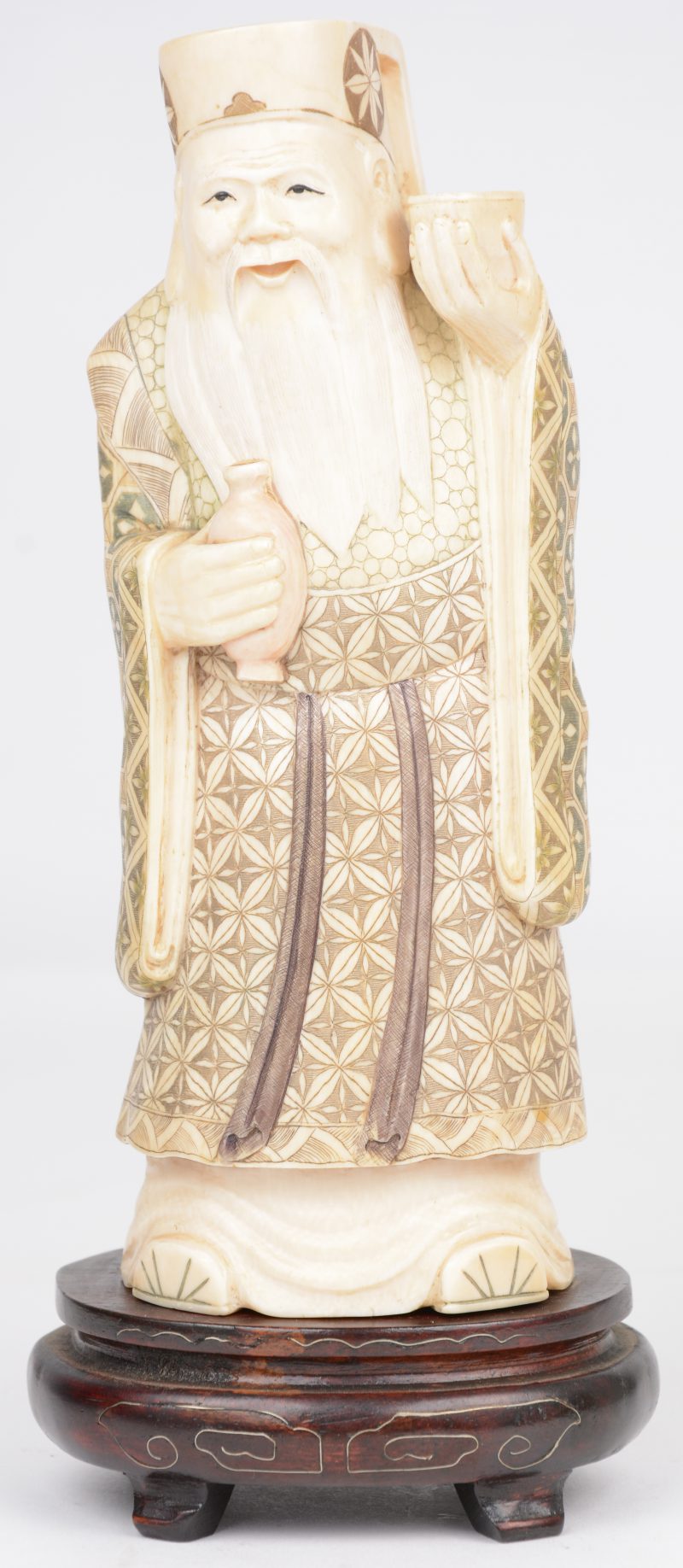 “Chinese wijze”. Een beeldje van gesculpteerd en deels gepolychromeerd ivoor op een ingelegd houten voetstukje. Onderaan gesigneerd.