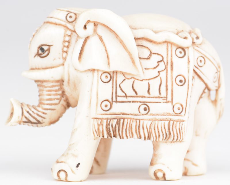 “Opgetuigde olifant”. Netsuké van gebeeldhouwd ivoor. Japan, eerste kwart XXste eeuw. Onderaan gemerkt.