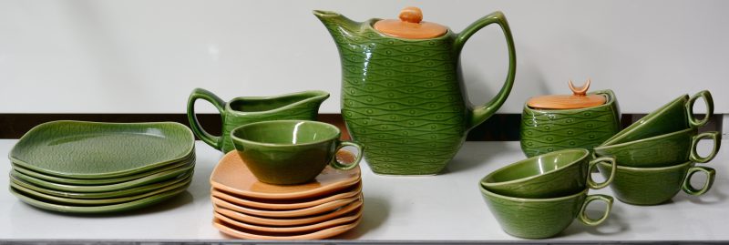 Een theeserviesje van groen en beige aardewerk, bestaande uit een theepot,  suikerpot en melkkannetje. Met kopjes en bordjes voor zes personen. Eén oortje gerestaureerd. Onderaan gemerkt. 1961.