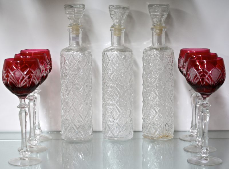 Een reeks van zes wijnglazen van geslepen rood Boheems kristal. We voegen er drie kleurloze glazen karaffen aan toe.