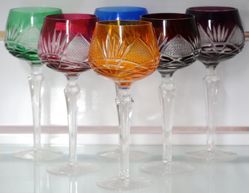 Een reeks van zes gekleurde wijnglazen van geslepen kristal.