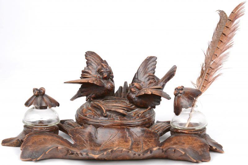 Een gebeeldhouwd houten bureautelletje met twee glazen inktpotten en een doosje, versierd met twee vogeltjes bij een nest op het deksel.