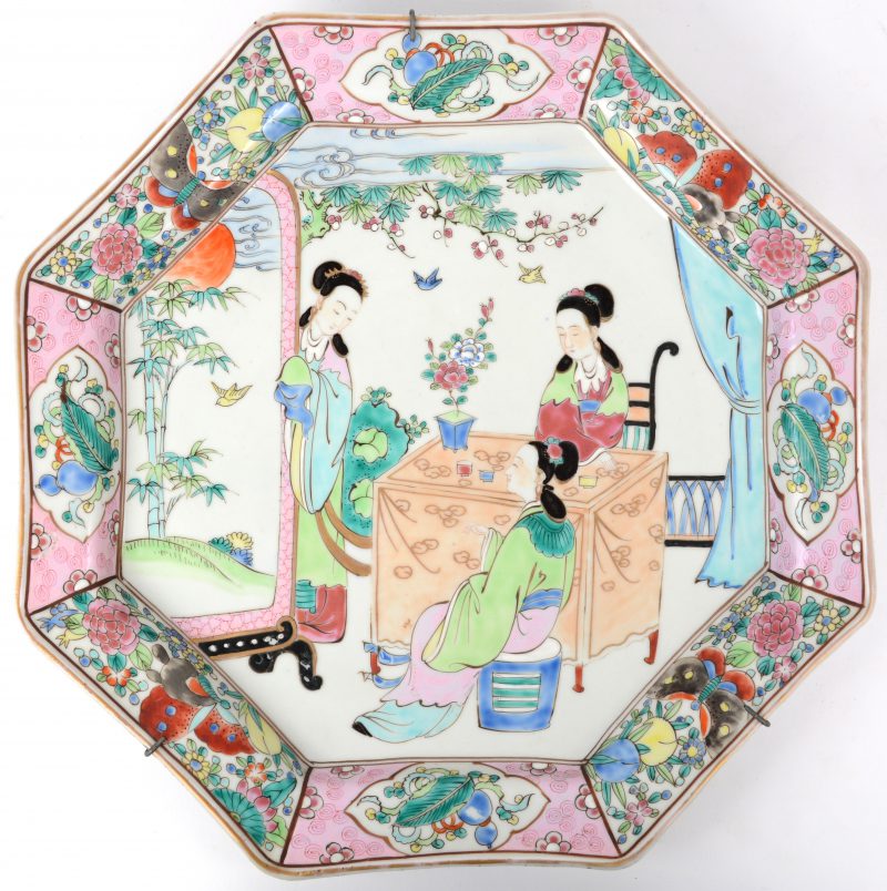 Een achthoekig bord van Chinees porselein met een famille-rosedecor van kange lijzen aan een tafel.