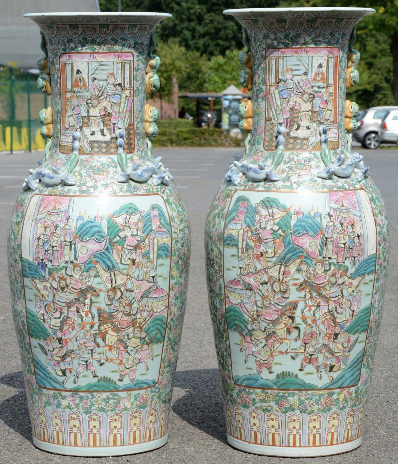 Een paar grote balustervazen van Chinees porselein met een meerkleurig decor van de Keizerlijke hofhouding in cartouches in een celadonkleurige achtergrond van bloemen, fruit en vogels. De hals en de schouder versierd met fabeldieren in hoofreliëf.