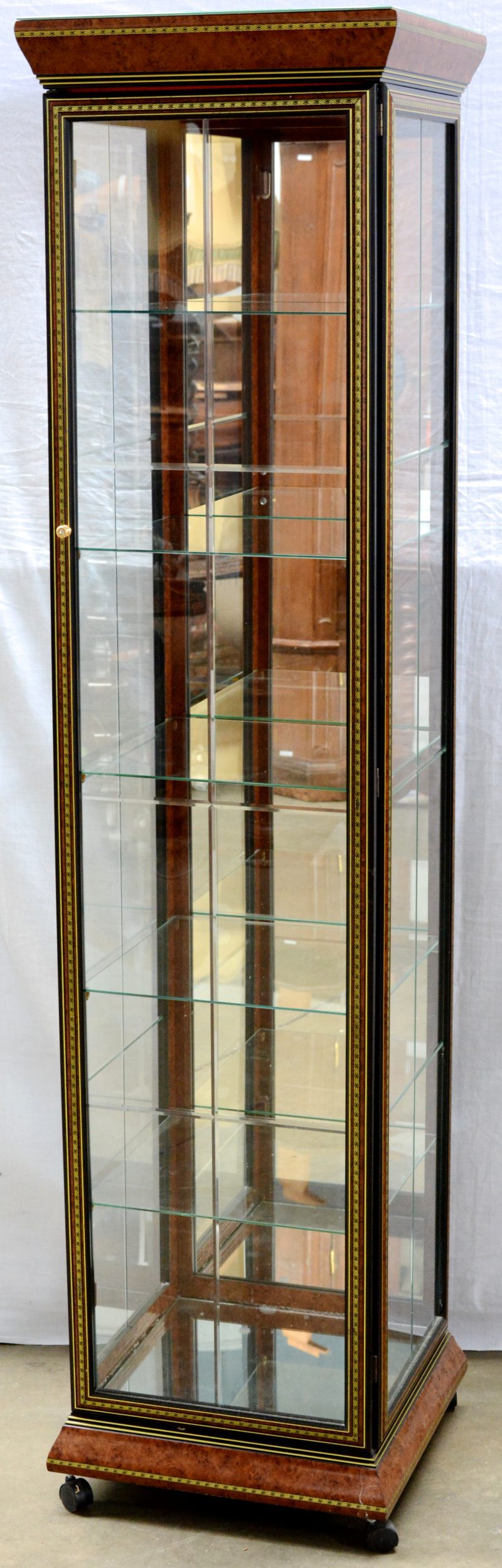 Een Italiaanse kolomvitrine op wieltjes met vijf glazen leggers en versierd met imitatie wortelnootfineer.